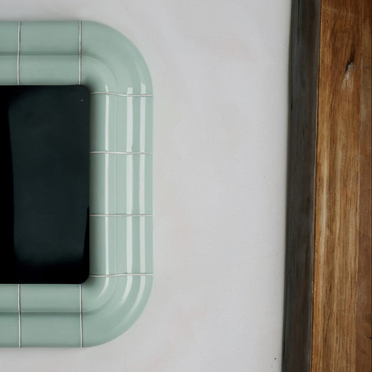 Soft green square mirror with visible joints and rounded geometry, presented as a standalone wall object.