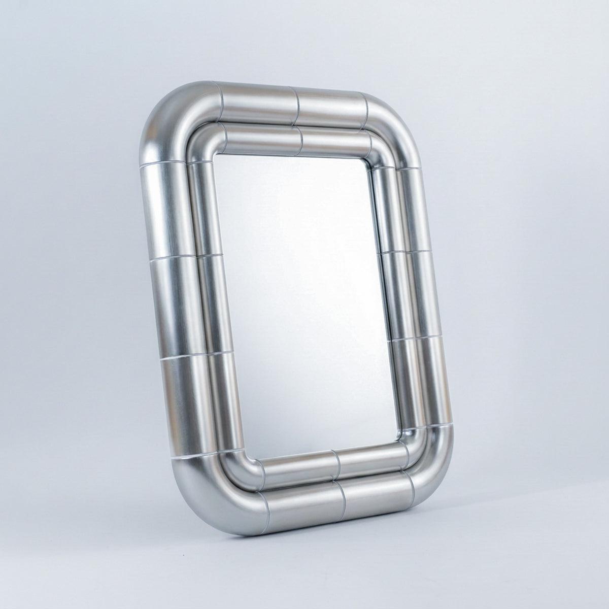 Three-quarter view of the Portalito mirror in Steel finish standing upright, revealing the depth of its doubled metallic frame