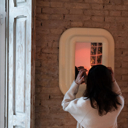 Person adjusting their hair in a Soft Butter ceramic-look mirror installed on a brick wall.