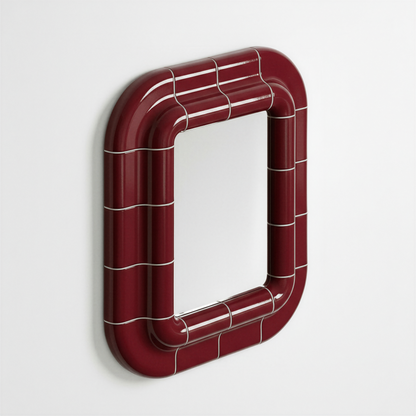 Deep burgundy ceramic-inspired mirror mounted on wall, shown in angled perspective highlighting its curved frame and glossy surface.