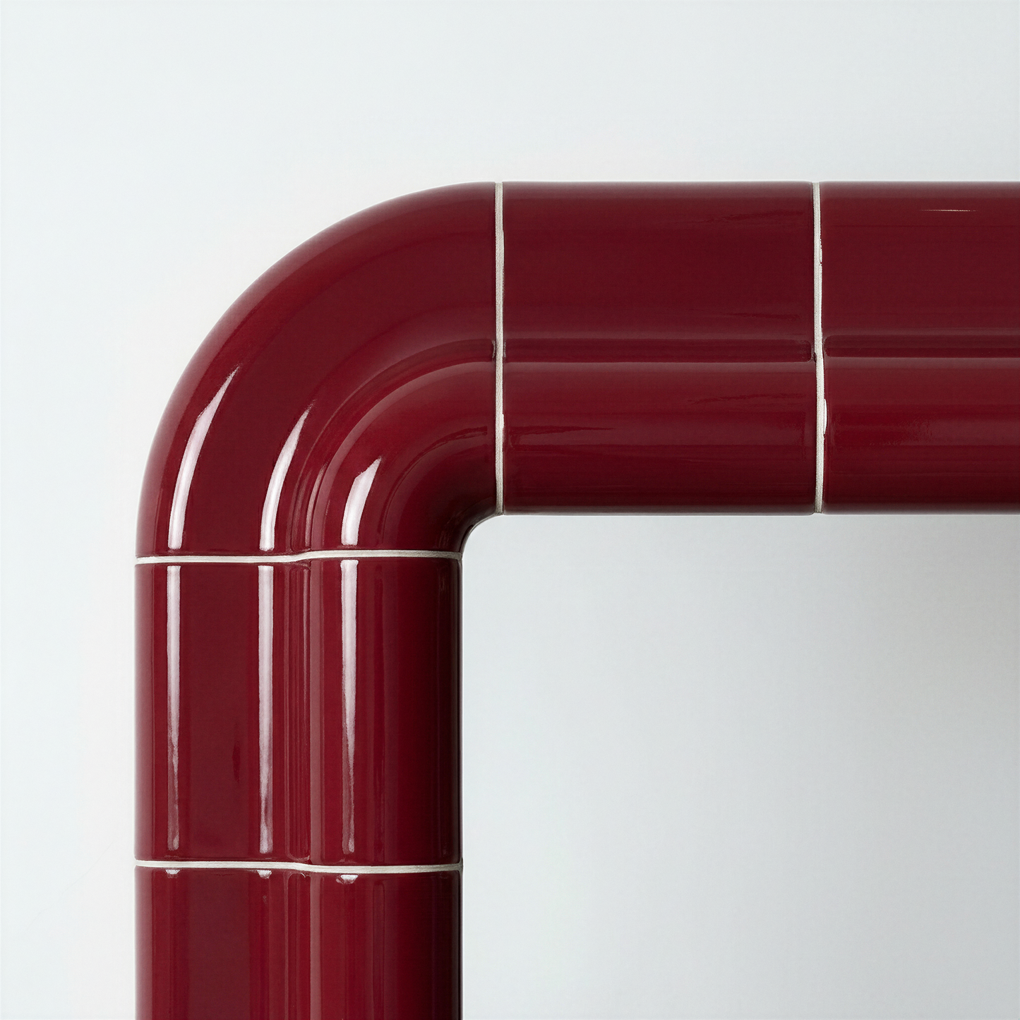 Close-up of the rounded corner of a deep burgundy ceramic-look mirror, showing glossy finish and visible joint lines.