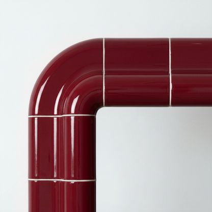 Close-up of the rounded corner of a deep burgundy ceramic-look mirror, showing glossy finish and visible joint lines.