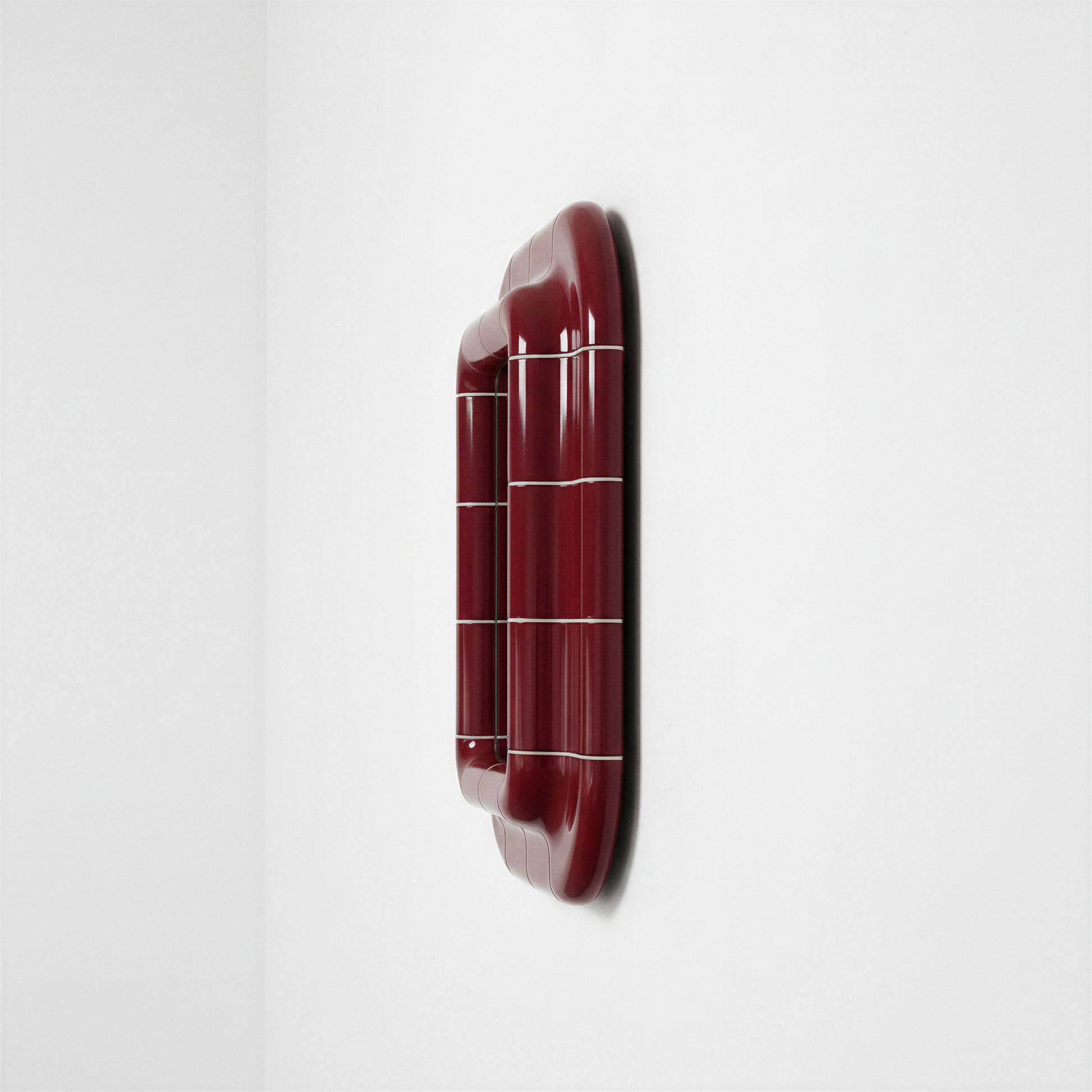 Side profile view of a deep burgundy ceramic-inspired mirror, emphasizing its thickness, curved volume, and glossy finish.