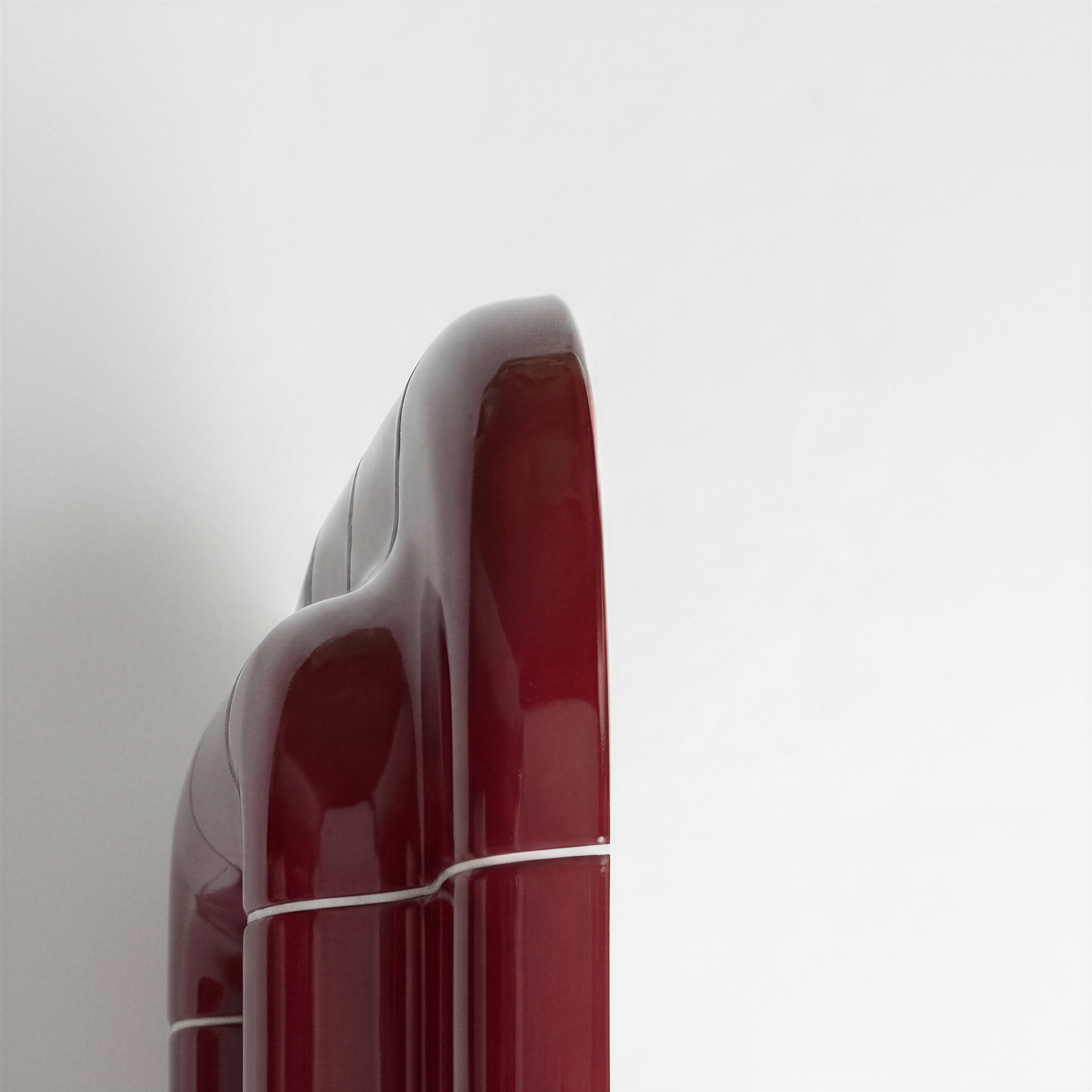 Detail view of the side edge of a deep burgundy mirror, highlighting the smooth ceramic-like surface and rounded geometry.