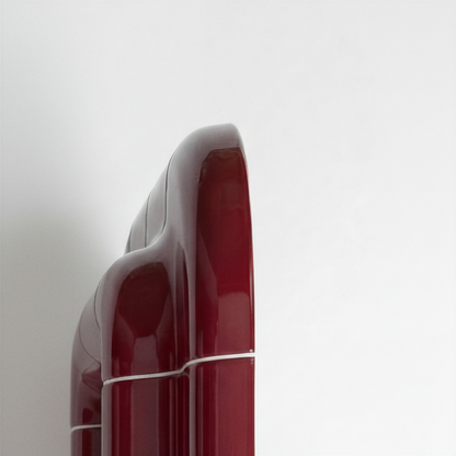 Detail view of the side edge of a deep burgundy mirror, highlighting the smooth ceramic-like surface and rounded geometry.