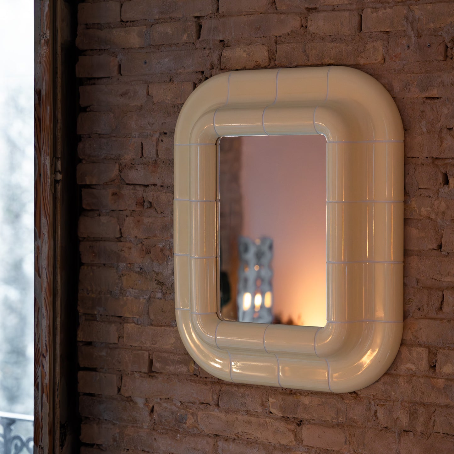 Soft Butter ceramic-look mirror mounted on a textured brick wall, reflecting warm ambient light.