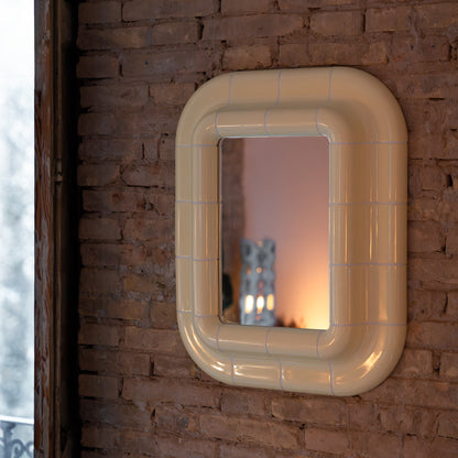 Soft Butter ceramic-look mirror mounted on a textured brick wall, reflecting warm ambient light.
