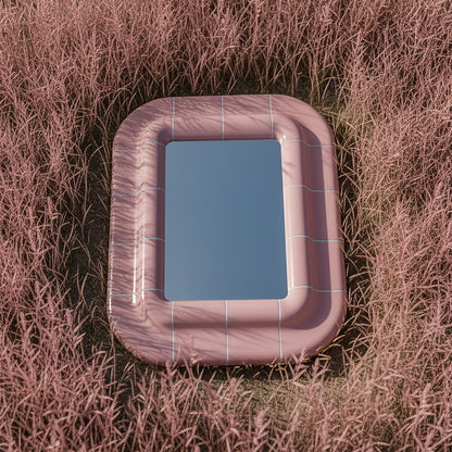 Top view of a pink sculptural mirror with soft curves and glossy finish, surrounded by pink grass, highlighting its shape and reflective glass.