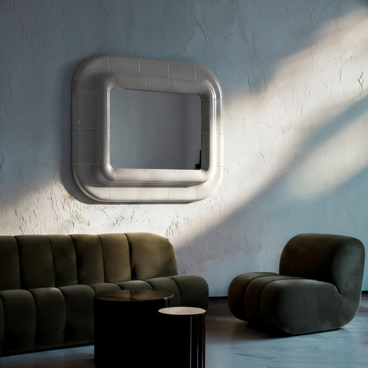 Wall-mounted square mirror with rounded corners and smooth glossy surface, interacting with light and shadow in a minimalist interior.