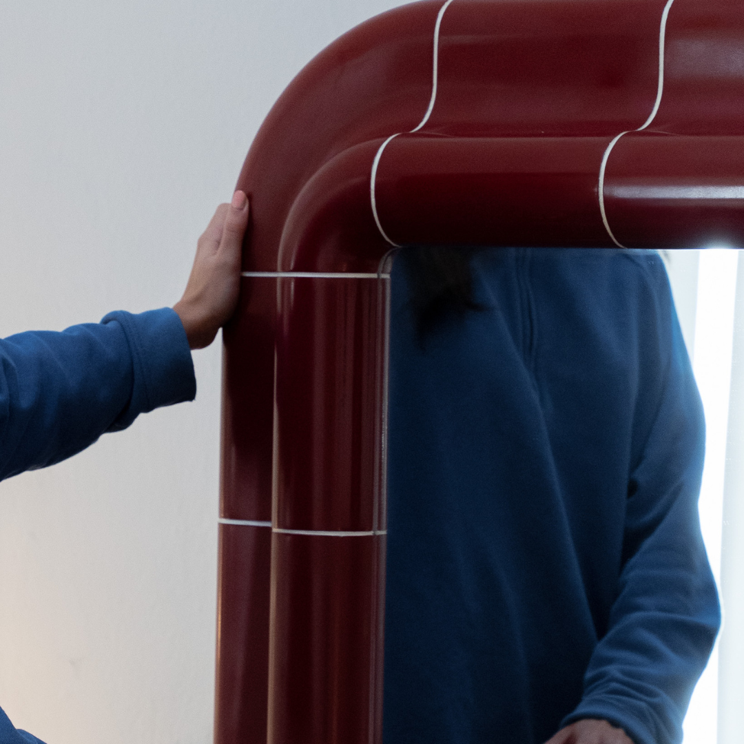 Lola Mirror in Deep Burgundy reflected in a contemporary interior with a person standing nearby.