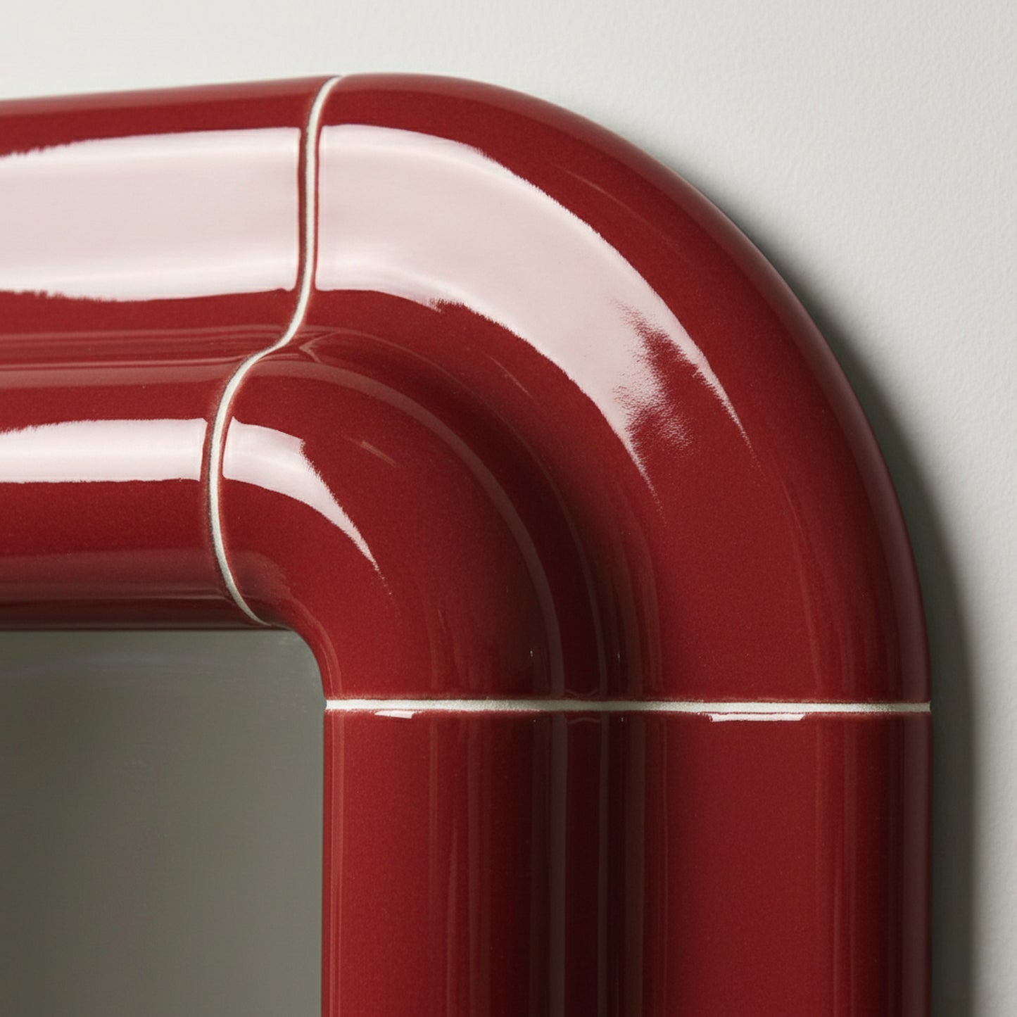 Close-up of Lolo ceramic mirror frame in deep burgundy high-gloss finish showing rounded corner detail and tile joints.