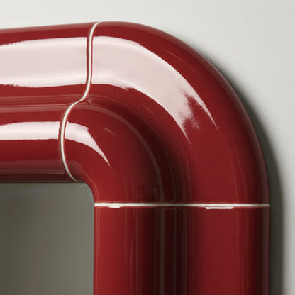 Close-up of Lolo ceramic mirror frame in deep burgundy high-gloss finish showing rounded corner detail and tile joints.