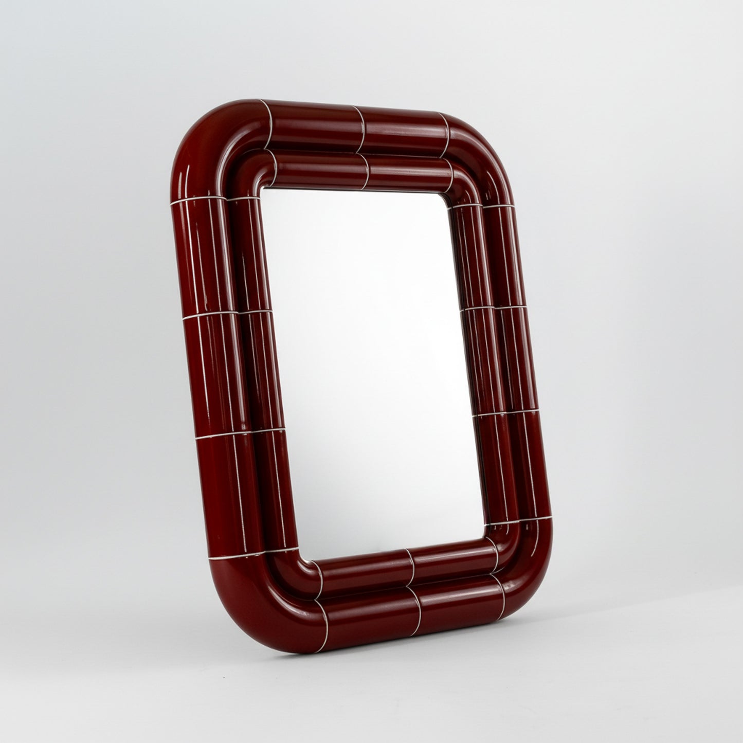 Portalito mirror in Deep Burgundy, sculptural tubular frame, angled view highlighting depth