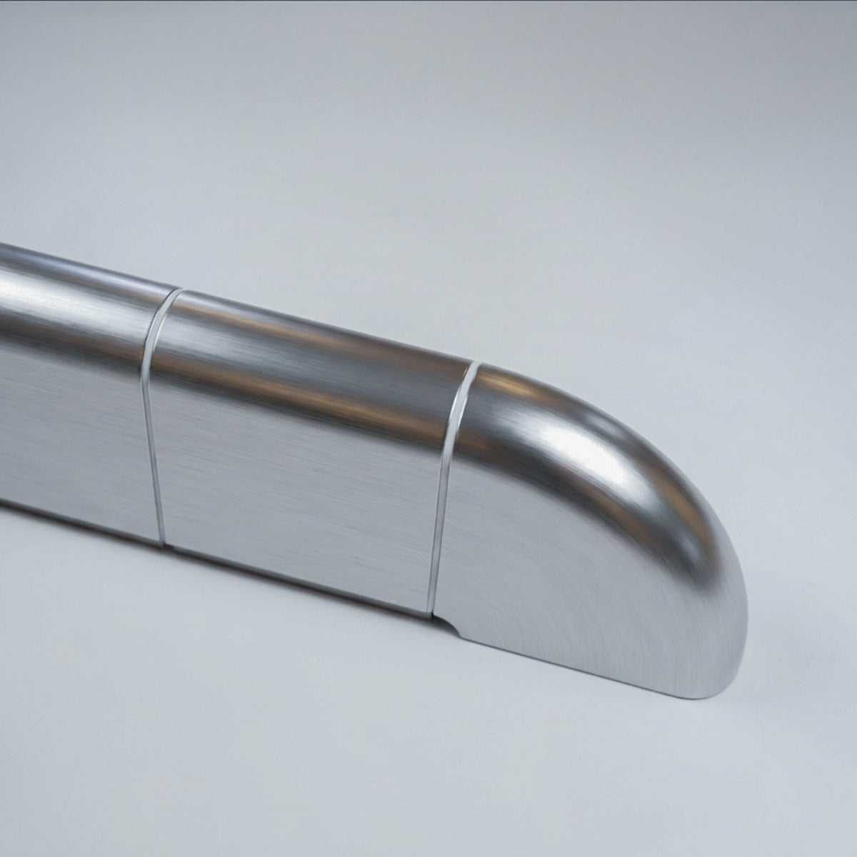 Close-up of the rounded end of the Orbi shelf, polished metallic finish with white grout joints
