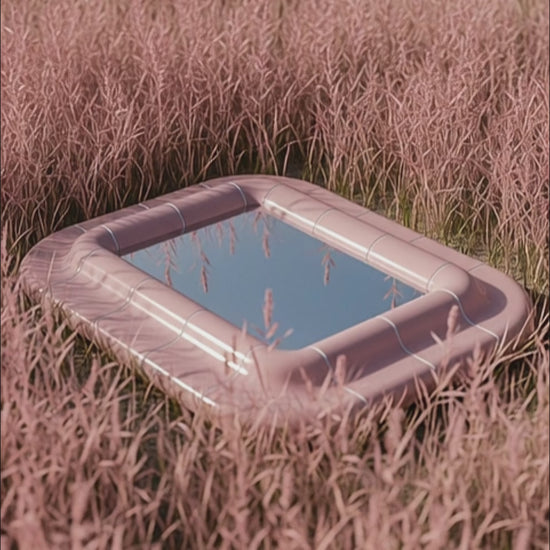 Lolita rounded mirror in Blush Pink high-gloss lacquer lying in tall grass, reflecting the sky